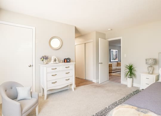 A white bedroom with a grey bed and a white chair.