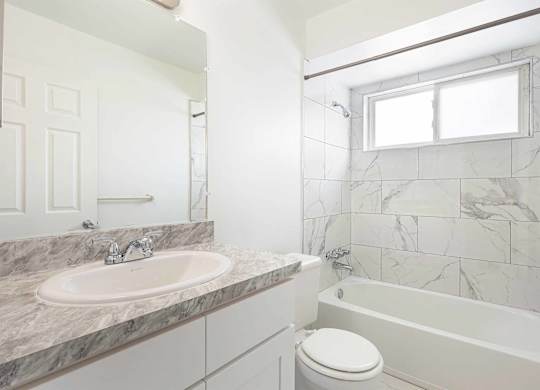 A white bathroom with a marble countertop and a white toilet.