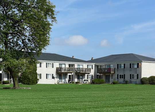 A large grassy field in front of a building with a tree on the left.