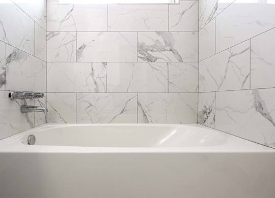 A white bathtub with a marble tile wall behind it.