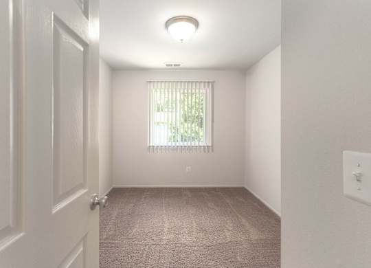 A room with a carpeted floor and a window with blinds.