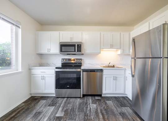 A kitchen with white cabinets and a wood floor.