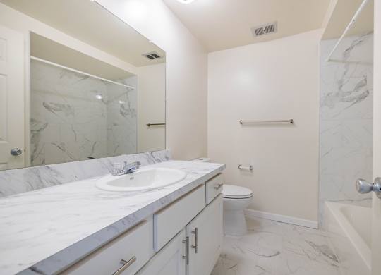 A white bathroom with a marble counter top and a toilet in the corner.