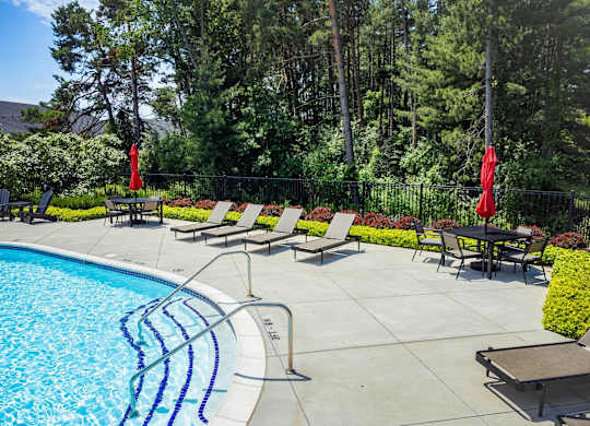 A pool surrounded by trees and chairs.