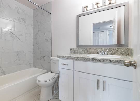 A white bathroom with a marble counter top and a large mirror.