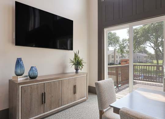 A black TV is mounted on a wall above a wooden cabinet with two doors and a shelf with three blue vases and a green plant.
