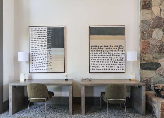 Two desks with chairs and lamps in front of a stone wall.