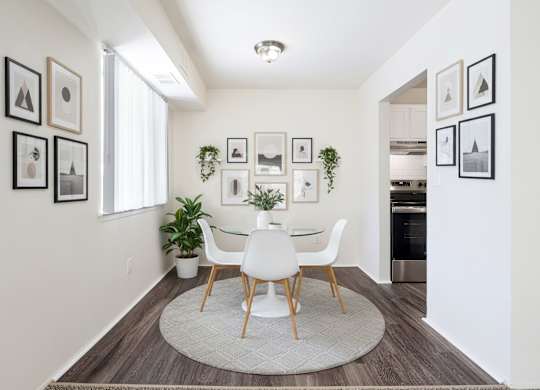 A white dining table with four chairs is in the middle of a room with a rug on the floor.