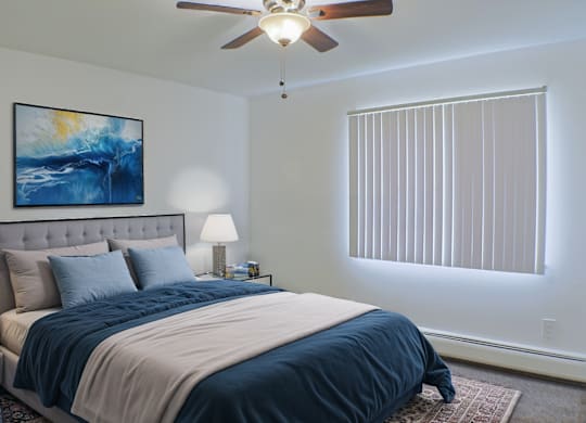 A bedroom with a bed, a ceiling fan, and a painting on the wall.