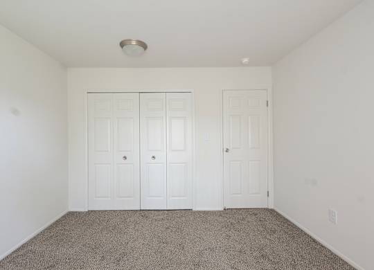 A room with two white doors and carpeted floor.