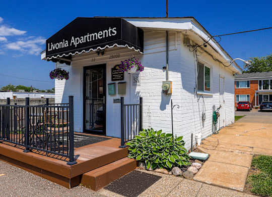 A white building with a black fence and a sign that says Livonia Apartments.