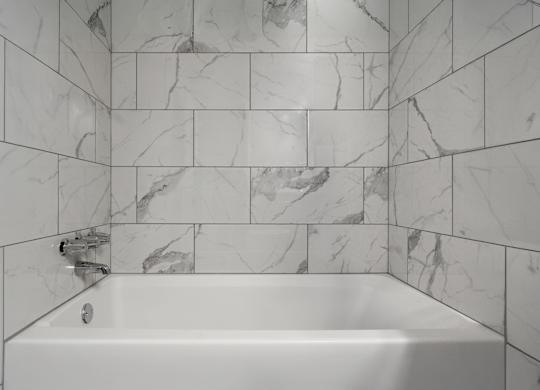 A white bathtub with a marble tile wall.