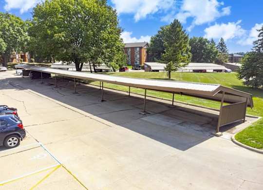 A long outdoor picnic table is surrounded by a parking lot.