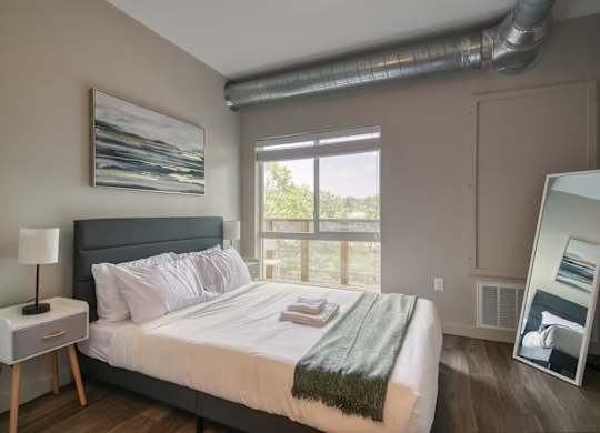 A bedroom with a bed, nightstand, and a painting on the wall.