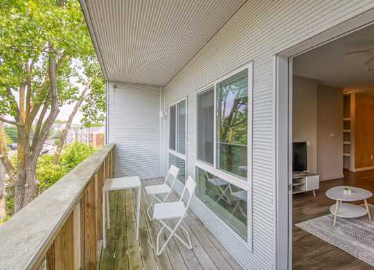 A balcony with a table and chairs overlooks a tree.