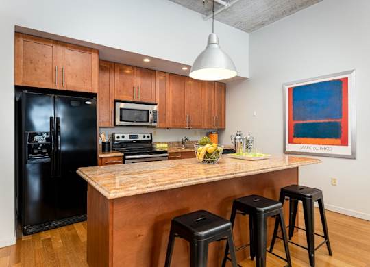 A kitchen with a black fridge, wooden cabinets, and a granite countertop.
