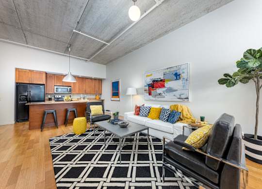 A living room with a black and white rug, a black couch, and a yellow pouf.