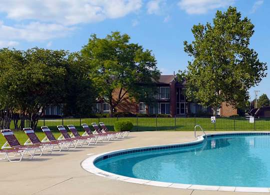 A pool surrounded by lawn chairs and trees.