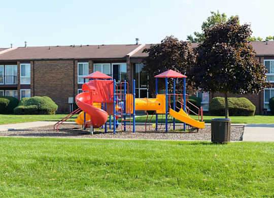 A playground with a red slide and yellow slide in front of a building.