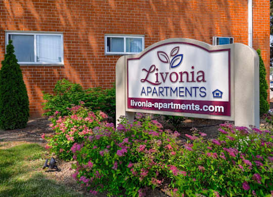 A sign for Livonia Apartments is displayed in front of a brick building.