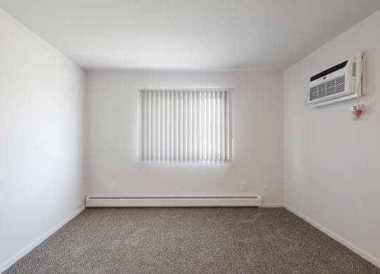 A room with a window covered by blinds and an air conditioner on the wall.