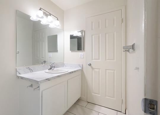 A white bathroom with a sink, mirror, and lighting fixture.