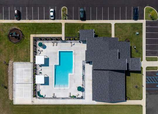 A swimming pool is surrounded by a tennis court and a building.