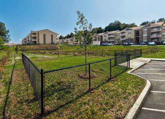 A black fence surrounds a green field with apartment buildings in the background.