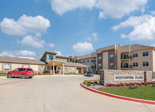 A red car is parked in front of a building named Whitewing Plate.