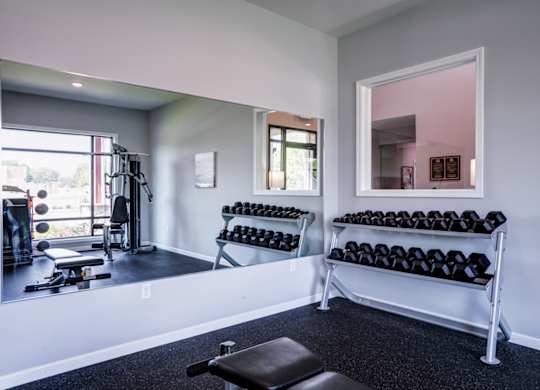 A gym room with a mirror, dumbbells, and a bench.