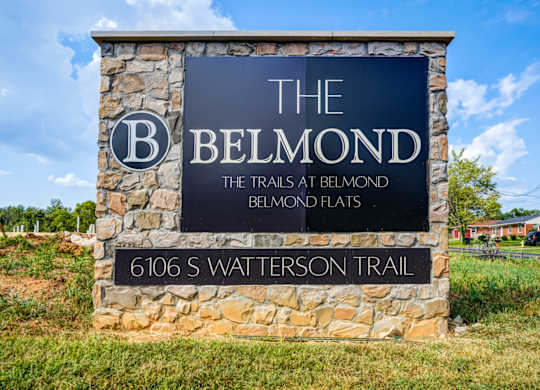 A sign for The Belmond Trails at Belmond Flats stands in front of a grassy area.