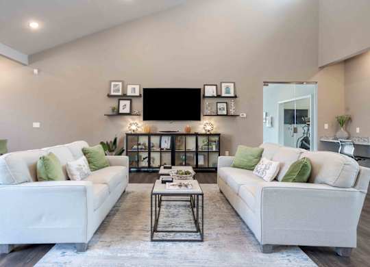 A modern living room with a white sofa set and a black television mounted on the wall.