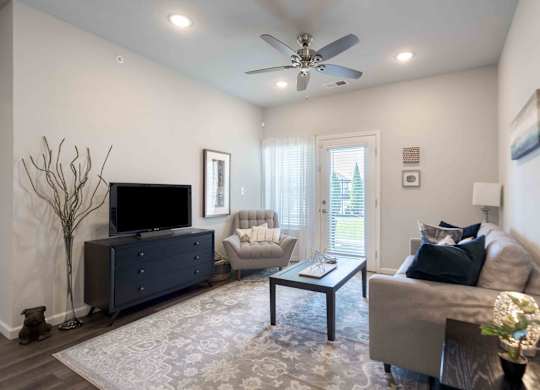 A living room with a grey couch, a black dresser, a television, and a ceiling fan.