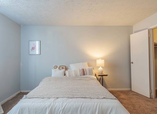 A bedroom with a bed, pillows, a nightstand, and a lamp.