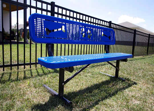 a blue bench in the grass in front of a fence