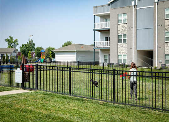 a girl is standing in a yard with a dog behind a fence