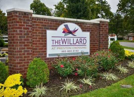 a sign for the willard at prestons crossing in front of a garden