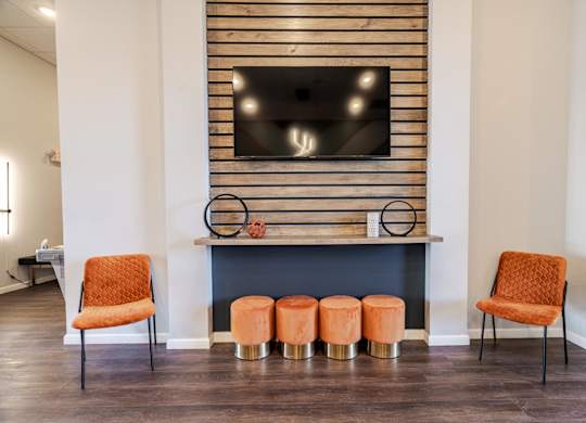 Two orange chairs are placed in front of a fireplace with a TV above it.