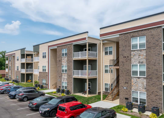 an exterior view of an apartment building with cars parked in a parking lot