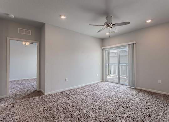 an empty room with a ceiling fan and a door to a balcony