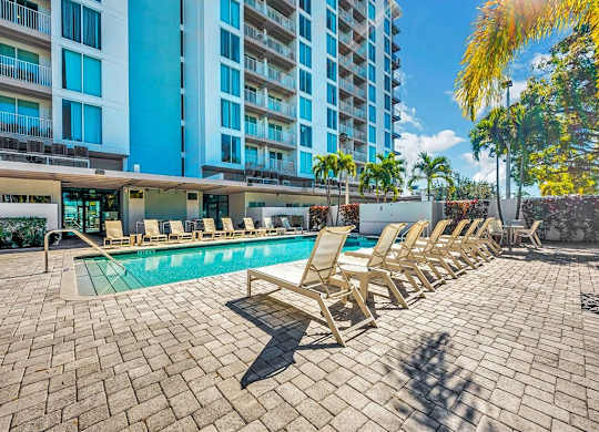 a swimming pool with chaise lounge chairs in front of a building at Elements on Third Apartments, St. Petersburg, FL, 33713