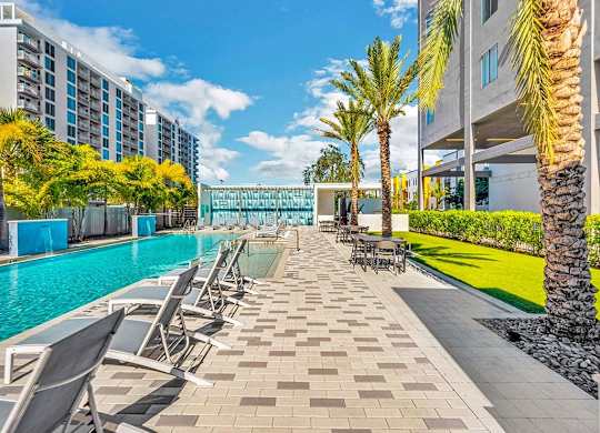 a swimming pool with chairs and palm trees in front of a building at Elements on Third Apartments, St. Petersburg, FL