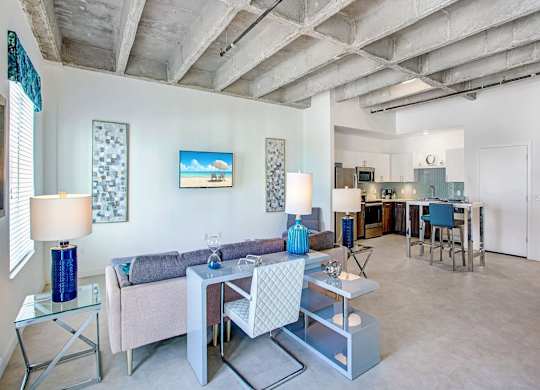 a living room with a couch and tables and a kitchen in the background at Elements on Third Apartments, Florida
