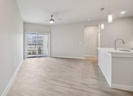 A spacious kitchen and living room with light wood flooring and white walls.