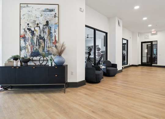 A large abstract painting hangs on a white wall above a black cabinet with a vase and a blue ball on top.