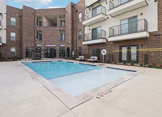 A pool in front of a brick building with balconies.