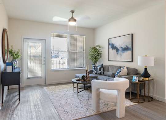 A living room with a grey couch, a white chair, and a painting on the wall.