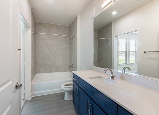 A white bathroom with a blue cabinet and a white tub.