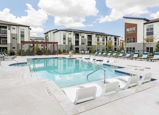 A swimming pool with lounge chairs in front of apartment buildings.