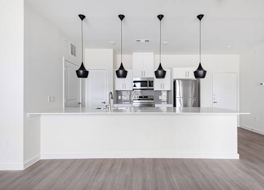 A modern kitchen with a white island and pendant lights.